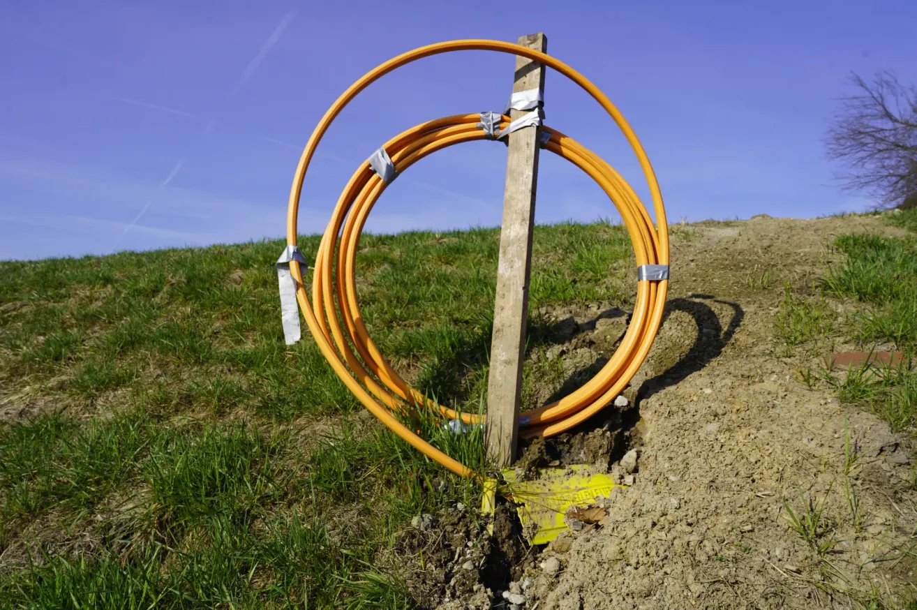 A wooden post with orange cables wrapped around it is buried in the ground on a grassy hill under a clear blue sky.