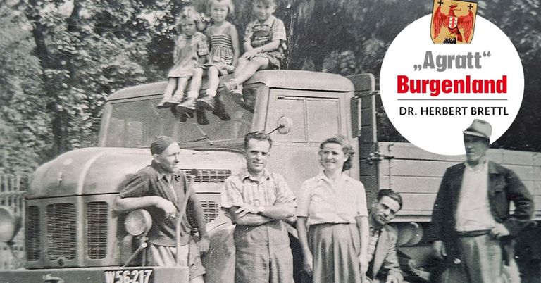 Ein altes Foto zeigt drei Kinder, die auf der Rückseite eines Trucks sitzen, mit vier Erwachsenen davor. Die Erwachsenen lächeln. Das Foto trägt den Titel Burg.