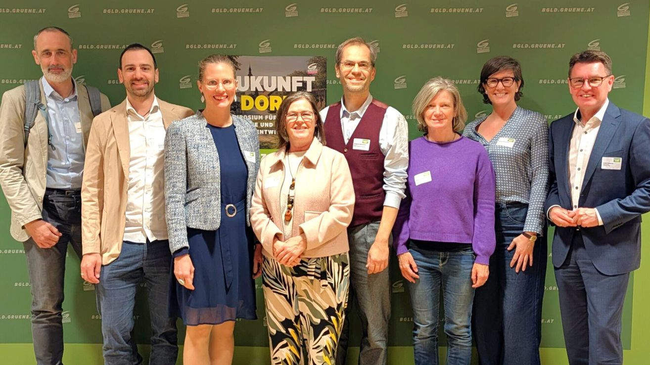 Fünf Personen posieren vor einem grünen Hintergrund mit einem Banner, das 'UKUNFT DOR' steht. Sie alle lächeln und schauen in die Kamera.