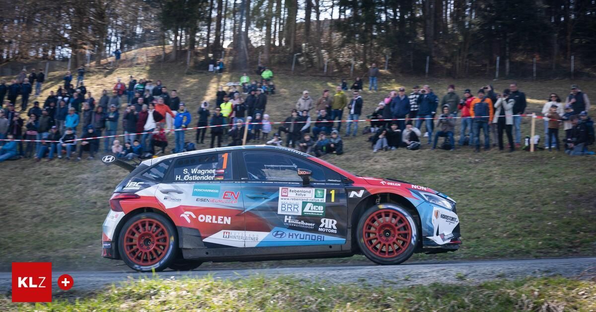 Ein Rallye-Auto fährt auf einer abschüssigen Straße, mit Zuschauern. Das Auto ist blau, weiß und rot mit einem Hyundai-Logo und wird von Orlen und anderen Marken gesponsert.