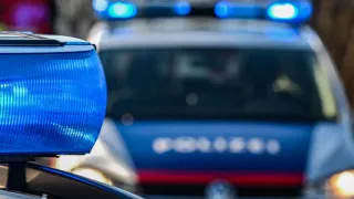 A police car is parked with its lights on. The car is blue and has white letters. The car is blurry.