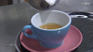 A close-up of a cup of coffee being poured from a silver pitcher into a blue cup on a pink saucer.