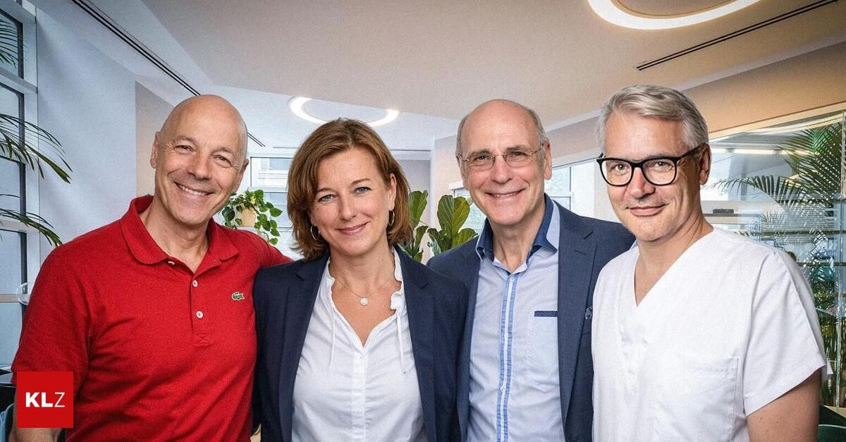 Four individuals pose for a photo in an office, with two men wearing glasses, one woman with a necklace, and a man in a red polo shirt.