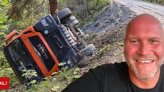 Ein großer orangefarbener und schwarzer Traktor ist auf einer schlammigen Straße umgestürzt, neben ihm steht ein lächelnder Mann.