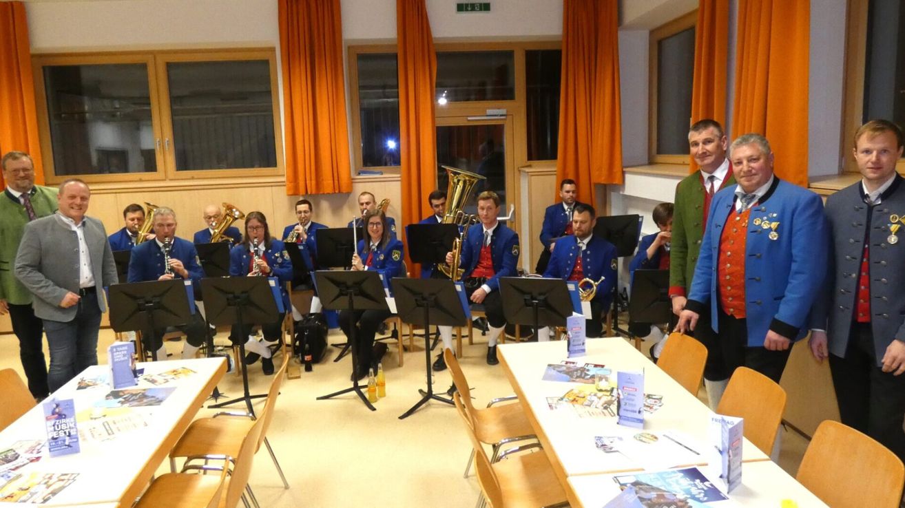 Eine Band spielt Instrumente in einem Raum mit Stühlen und Tischen. Sie sind in blauen Uniformen gekleidet.