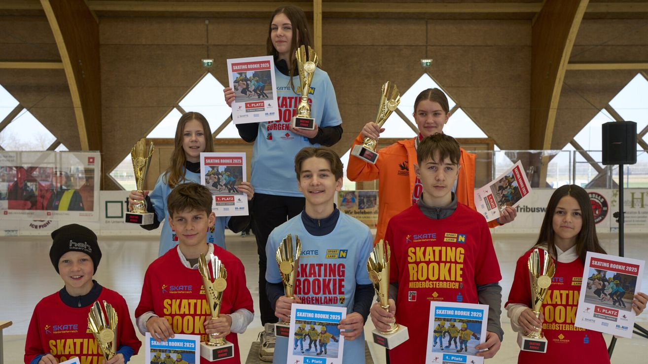 Mehrere junge Skater halten Pokale und Zeitschriften. Sie stehen in einer Gruppe. Sie tragen Trikots mit verschiedenen Texten und Zahlen. Sie lächeln und posieren für ein Foto.