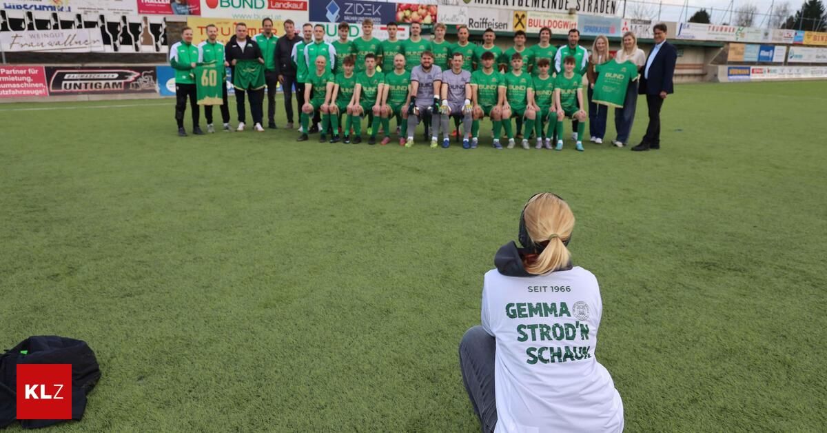 Eine Fußballmannschaft posiert auf einem Feld für ein Foto, mit einer knienden Frau im Vordergrund.