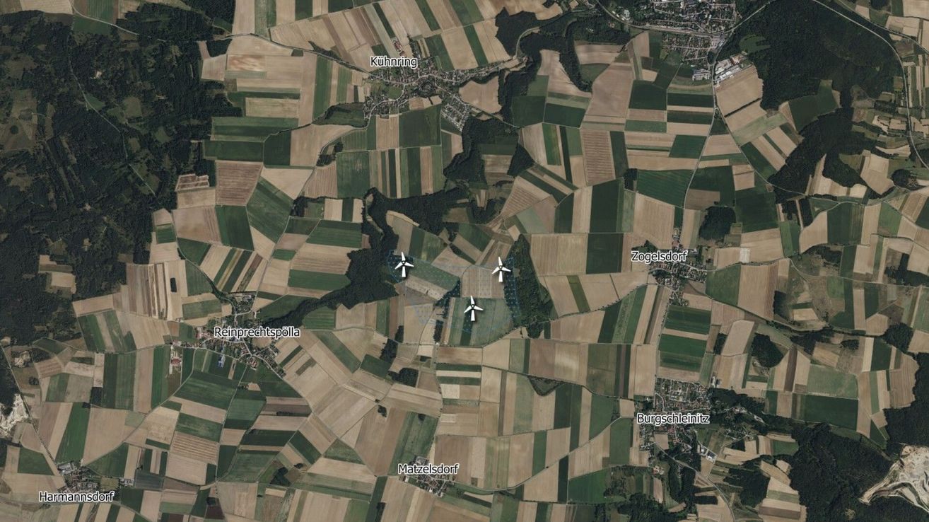 Luftaufnahme einer Landschaft mit verschiedenen Feldern und drei Windturbinen bei Reinprechtspölla, Kühnring, Matzersdorf und Zogelsdorf. Die Felder sind in rechteckige Parzellen unterteilt, wobei einige Bereiche Anzeichen einer kürzlichen Ernte aufweisen.