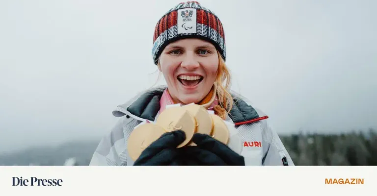 Eine Frau in einer Winterkleidung hält mehrere Goldmedaillen und lächelt fröhlich. Die Jacke trägt die Aufschrift 'AURI', und sie trägt eine Mütze mit 'Austria' darauf.