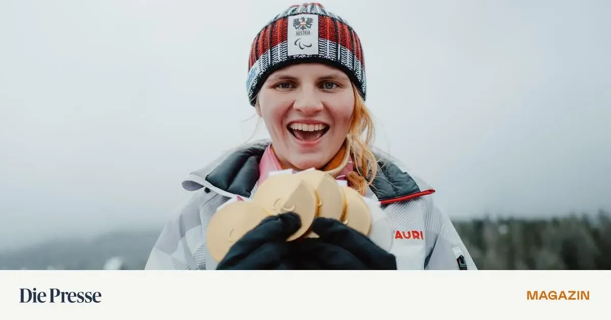 Eine Frau in einer Winterkleidung hält mehrere Goldmedaillen und lächelt fröhlich. Die Jacke trägt die Aufschrift 'AURI', und sie trägt eine Mütze mit 'Austria' darauf.