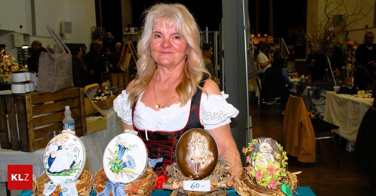Eine Frau in traditioneller Kleidung hält verzierte Eier, wahrscheinlich auf einem Festival. Hinter ihr sind verschwommene Menschen im Hintergrund zu sehen.