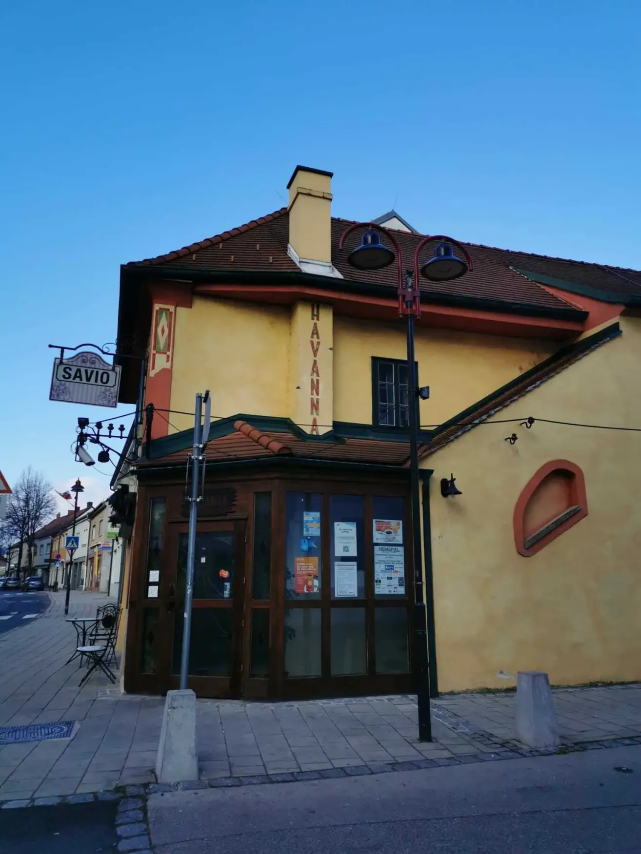 Ein gelbes Gebäude mit einem braunen Dach und Schornstein hat ein Schild, das Havanna liest. Eine Straßenlaterne und eine Bank stehen davor.