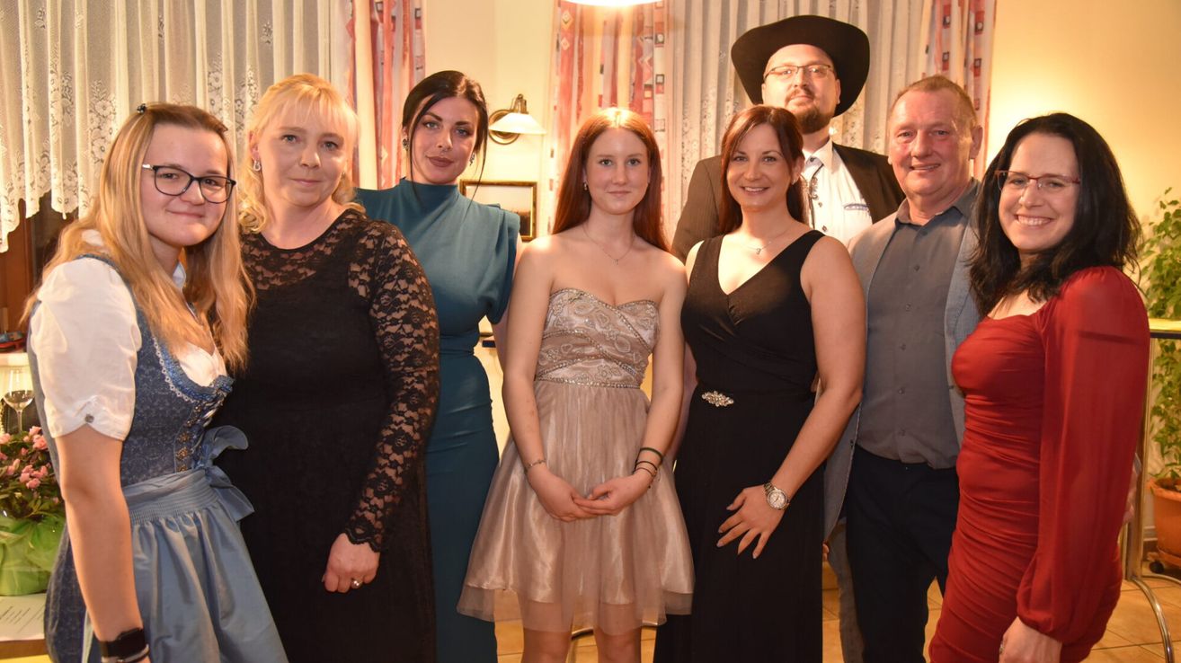 Eine Gruppe von Erwachsenen posiert für ein Foto, darunter eine Frau in einem braunen Kleid, zwei Frauen in schwarzen Kleidern und ein Mann in einem Anzug.