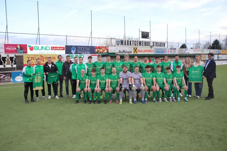 Eine Fußballmannschaft in grünen Trikots posiert für ein Gruppenfoto auf einem Feld mit Werbebannern im Hintergrund.