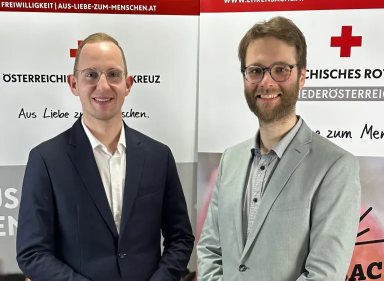 Zwei Männer in formeller Kleidung stehen nebeneinander, lächelnd, vor einem Schild, auf dem 'AUS-LIEBE-ZUM-MENSCHEN.AT' und 'WWW.EHRENACH.AT' steht.