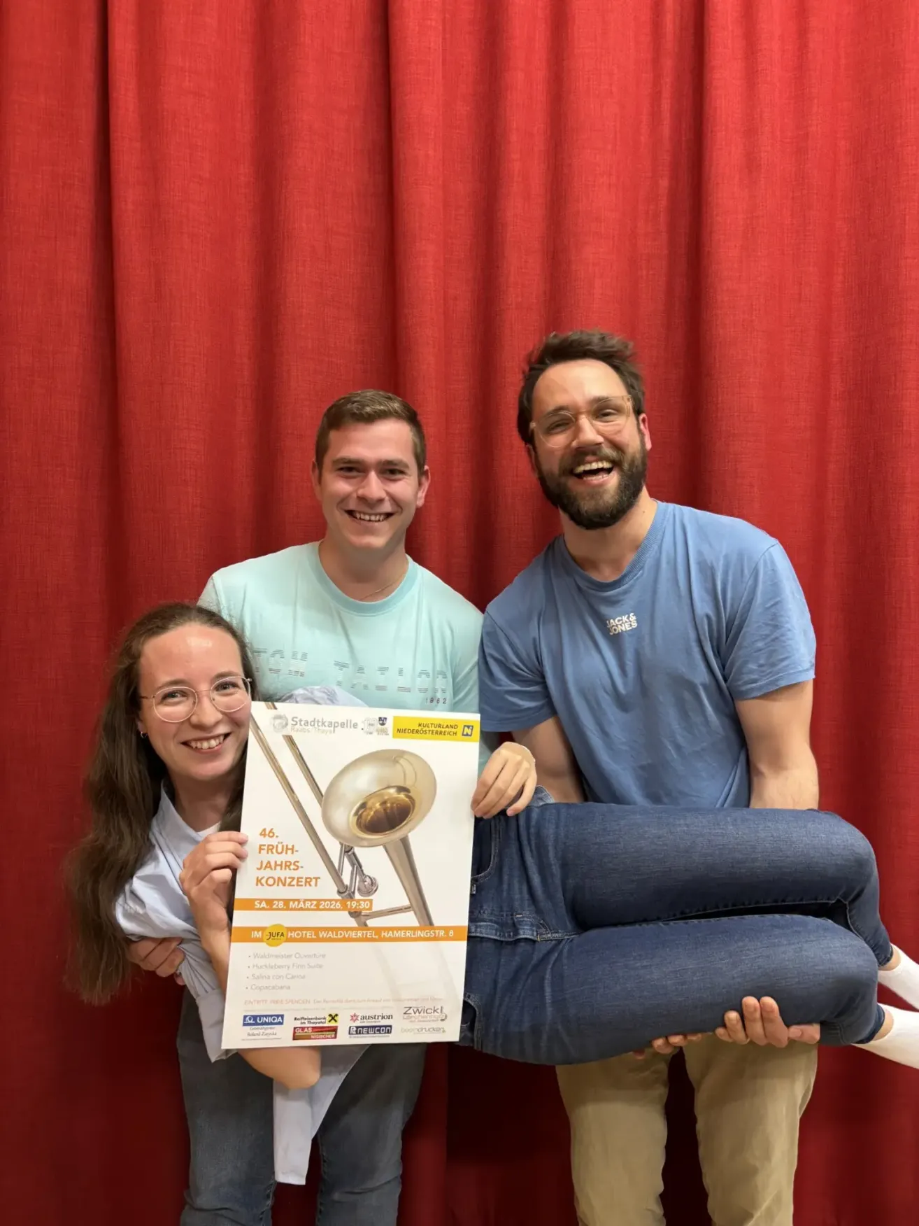 Drei Personen posieren für ein Foto mit einem Plakat, das ein Konzert in der Waldbühne Berlin am 28. März 2026 um 19:30 Uhr ankündigt.