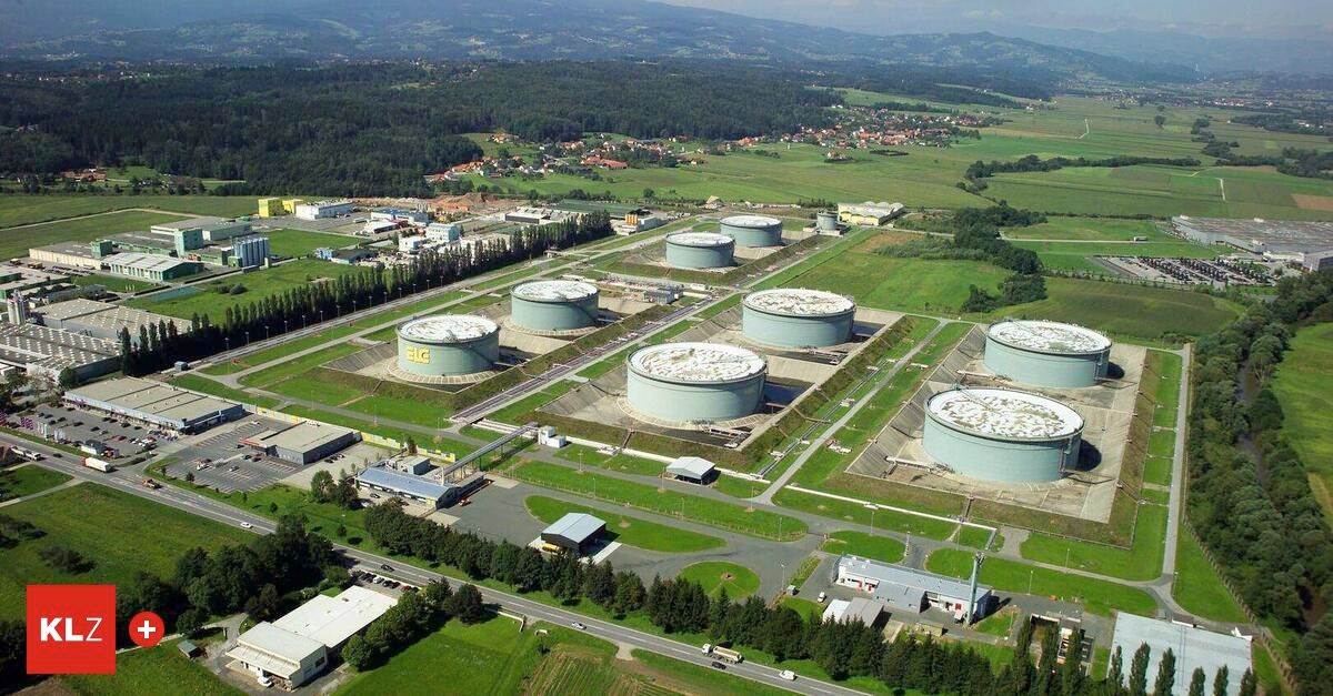 Luftaufnahme eines Industriekomplexes mit großen Lagertanks, umgeben von Grünflächen und Bergen in der Ferne.