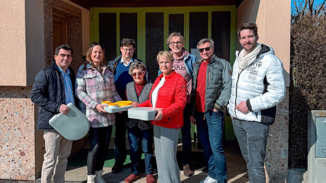 Eine Gruppe von Menschen, die zusammenstehen und Tabletts mit Essen halten, vor einem Gebäude mit einer grünen Tür.