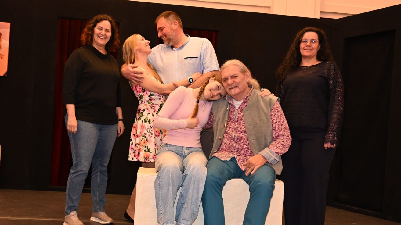 Eine Gruppe von Menschen, darunter ein Mann und zwei Frauen, posiert für ein Foto auf einer Bühne mit schwarzem Hintergrund.