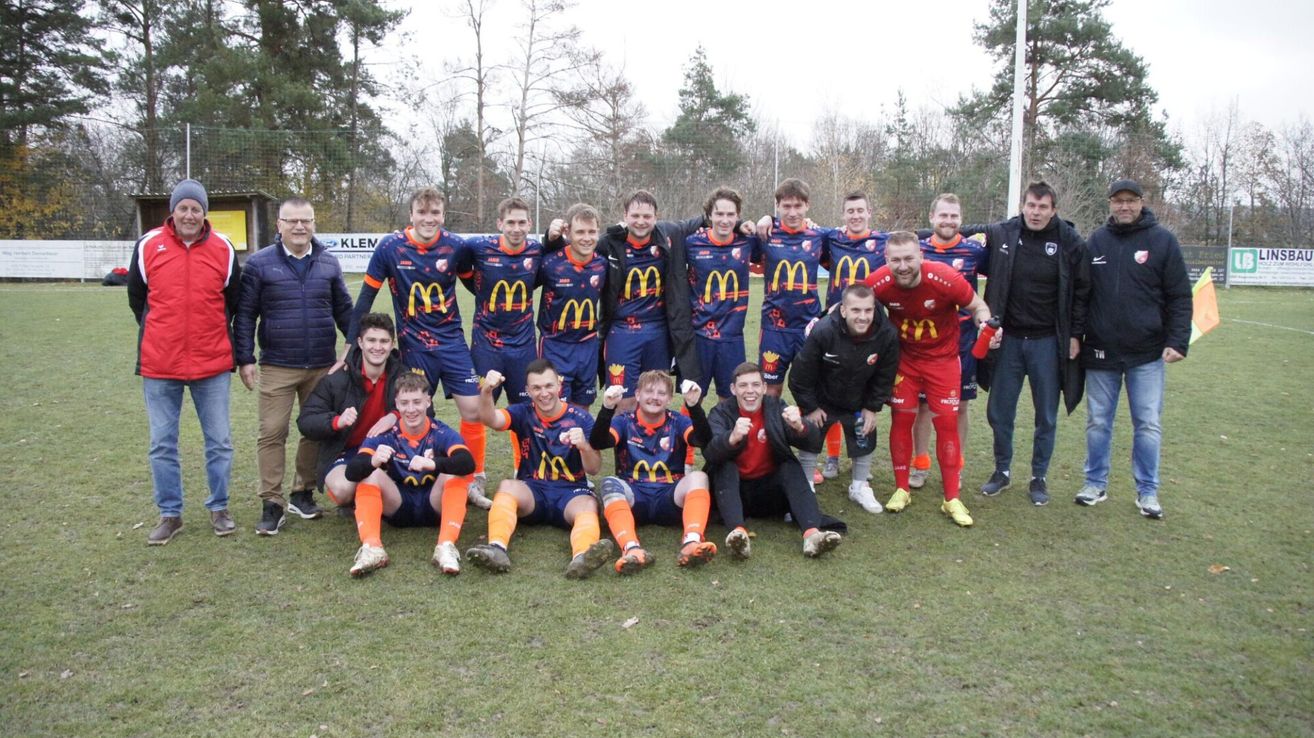Eine Rugby-Mannschaft in blauen Uniformen posiert für ein Mannschaftsfoto auf einem Rasenfeld mit einem McDonald's-Banner im Hintergrund.