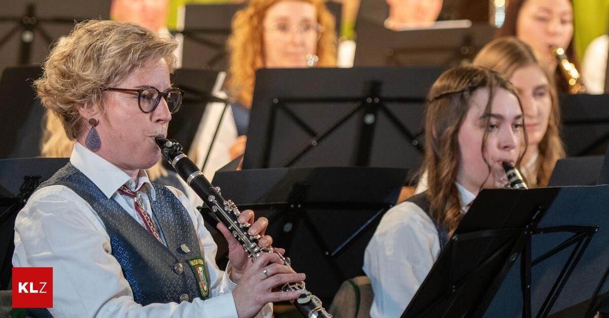Ein Musiker in einer Band spielt Klarinette, trägt eine Brille und eine Weste. Hinter ihm konzentrieren sich andere Bandmitglieder auf ihre Notenblätter.