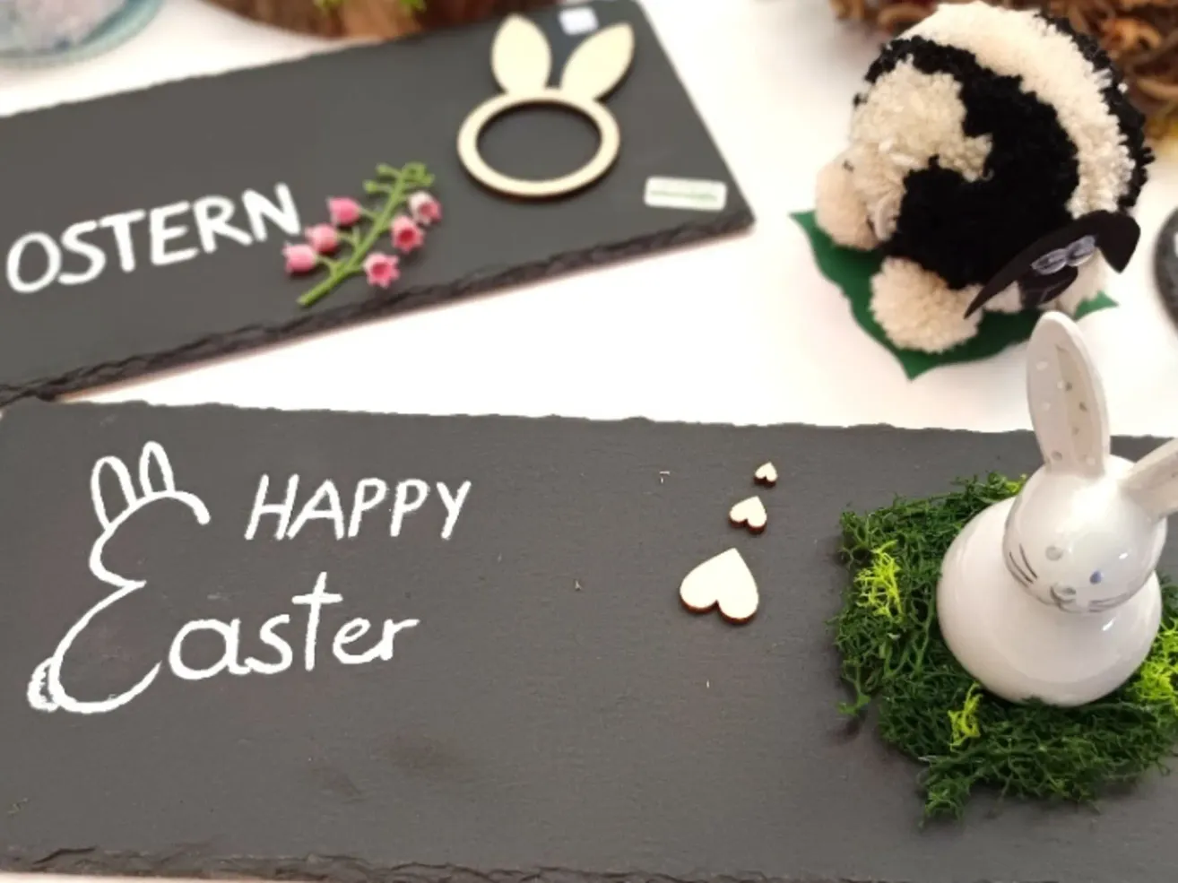 Ein Kreidetafel mit 'Frohes Ostern' darauf, einem Plüschtier und einem Schild mit 'ERN' und einem Hasenausschnitt.