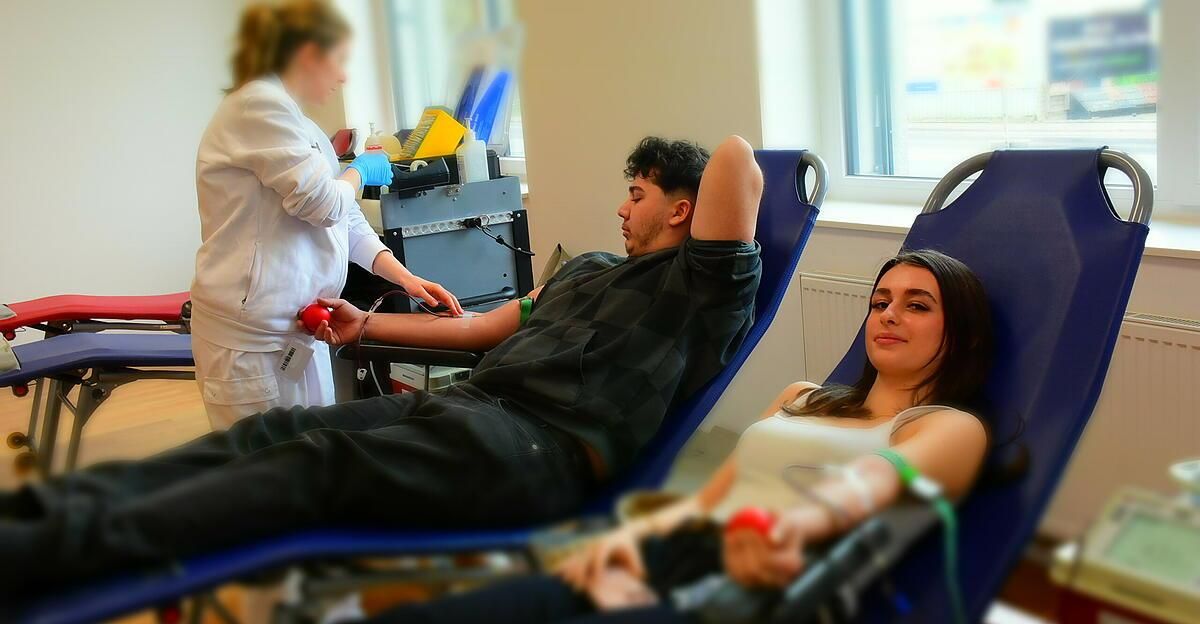 Ein Mann und eine Frau erhalten in einem Krankenhaus Blutspenden von einer Krankenschwester. Die Krankenschwester trägt einen weißen Kittel und Handschuhe.