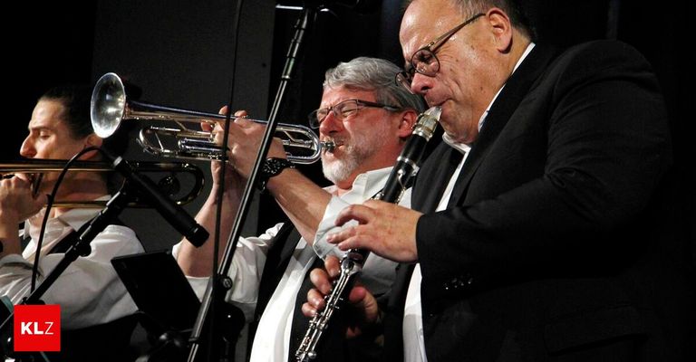 Zwei Musiker treten auf der Bühne auf. Der Mann auf der linken Seite spielt Trompete, während der Mann auf der rechten Seite Klarinette spielt.