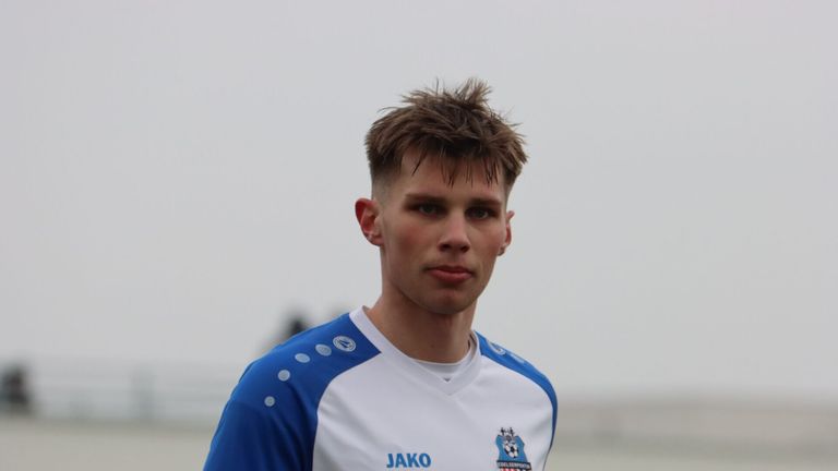 Ein Fußballspieler in einem blau-weißen Trikot mit dem Aufdruck Jako. Der Spieler steht auf einem Feld.