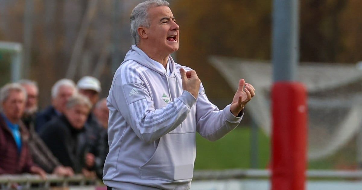 Ein Mann in einer weißen Adidas-Kapuzenjacke jubelt auf einem Feld, mit einer verschwommenen Menge hinter ihm.