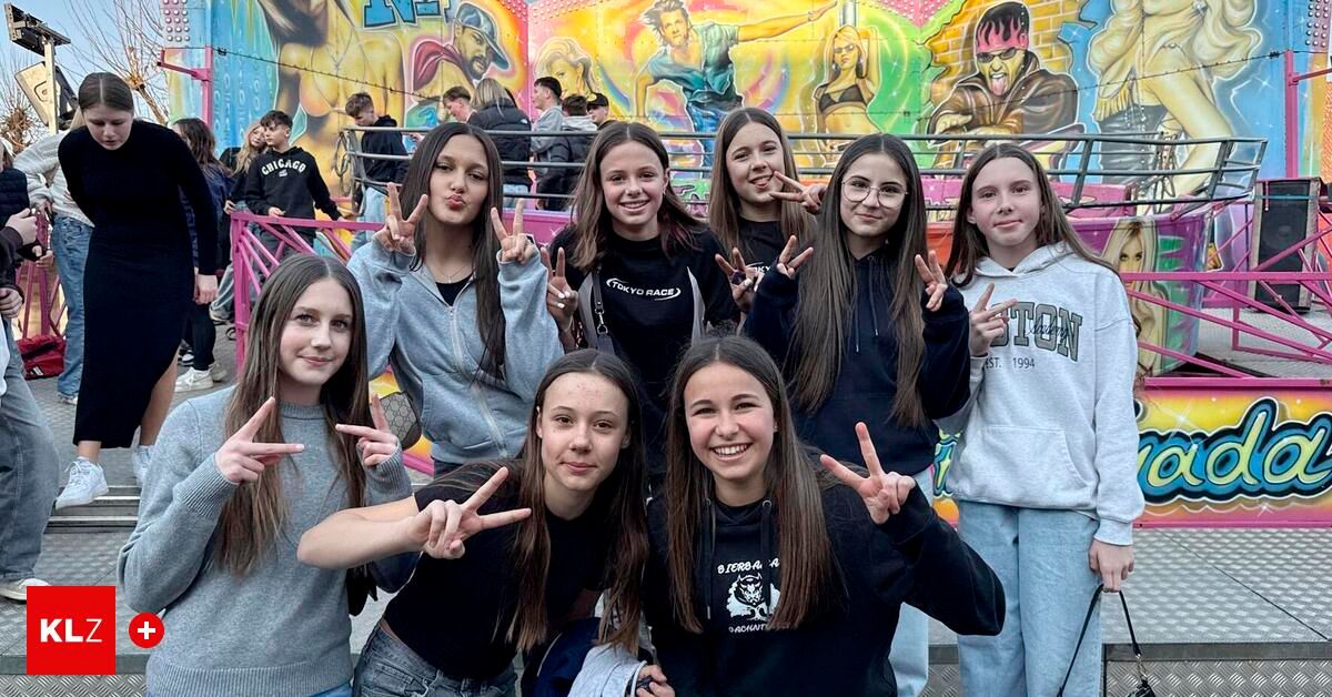 Eine Gruppe junger Frauen lächelt und posiert für ein Foto in einem Vergnügungspark mit bunten Graffiti an der Wand hinter ihnen.