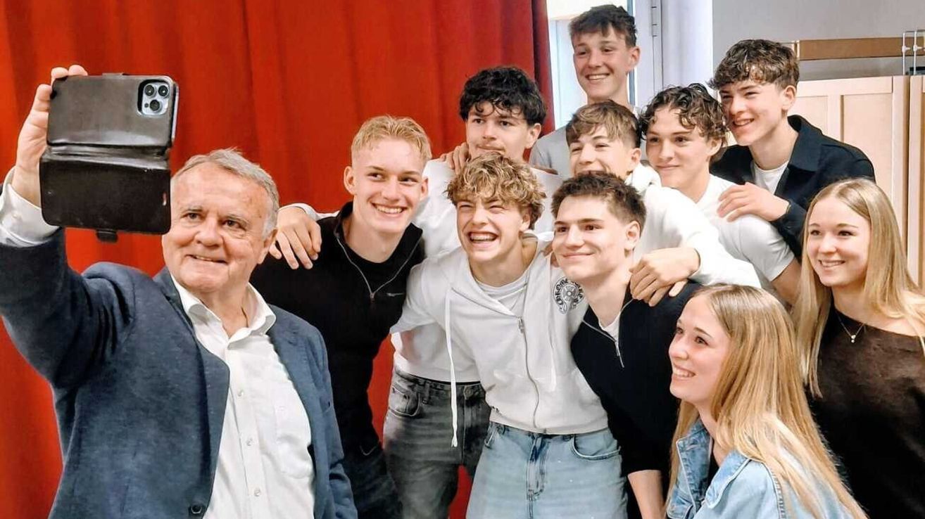 Eine Gruppe junger Menschen, darunter zwei Mädchen, lächelt und posiert für ein Foto vor einem roten Vorhang.