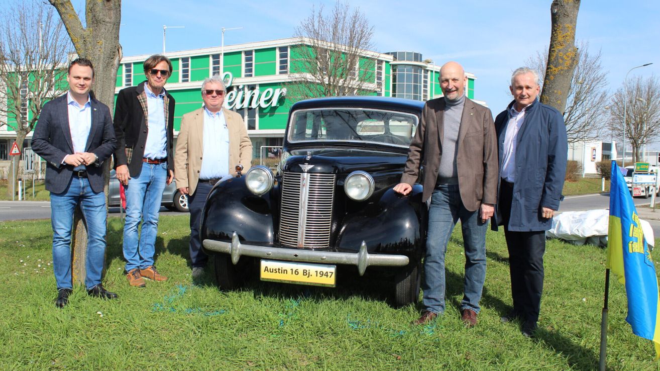 Vier Männer stehen neben einem Oldtimer Austin 16 Bj. 1947 auf einem Rasenfeld. Hinter ihnen steht ein Gebäude mit grüner und weißer Verkleidung.