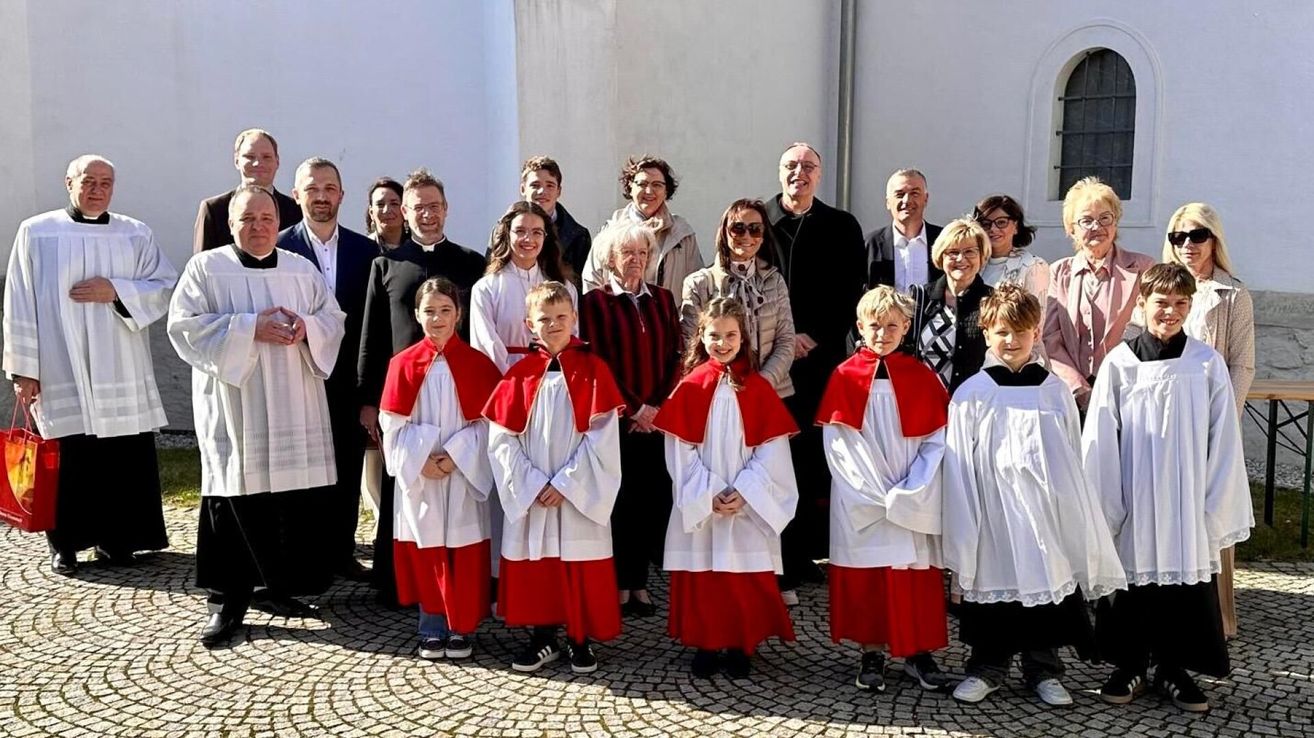 Eine Gruppe von Menschen, darunter Kinder in roten und weißen Gewändern, steht vor einem Gebäude. Sie posieren für ein Foto.