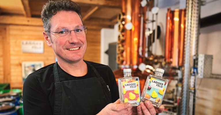 Ein Mann in einer schwarzen Schürze hält zwei Flaschen Laggers Field Spirit in einer Destillerie.