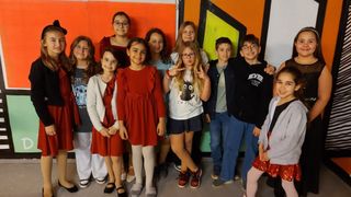 Eine Gruppe von Kindern, sowohl Jungen als auch Mädchen, stehen zusammen vor einer farbenfrohen Wand mit verschiedenen Farben und Formen. Sie alle lächeln und posieren für ein Foto.