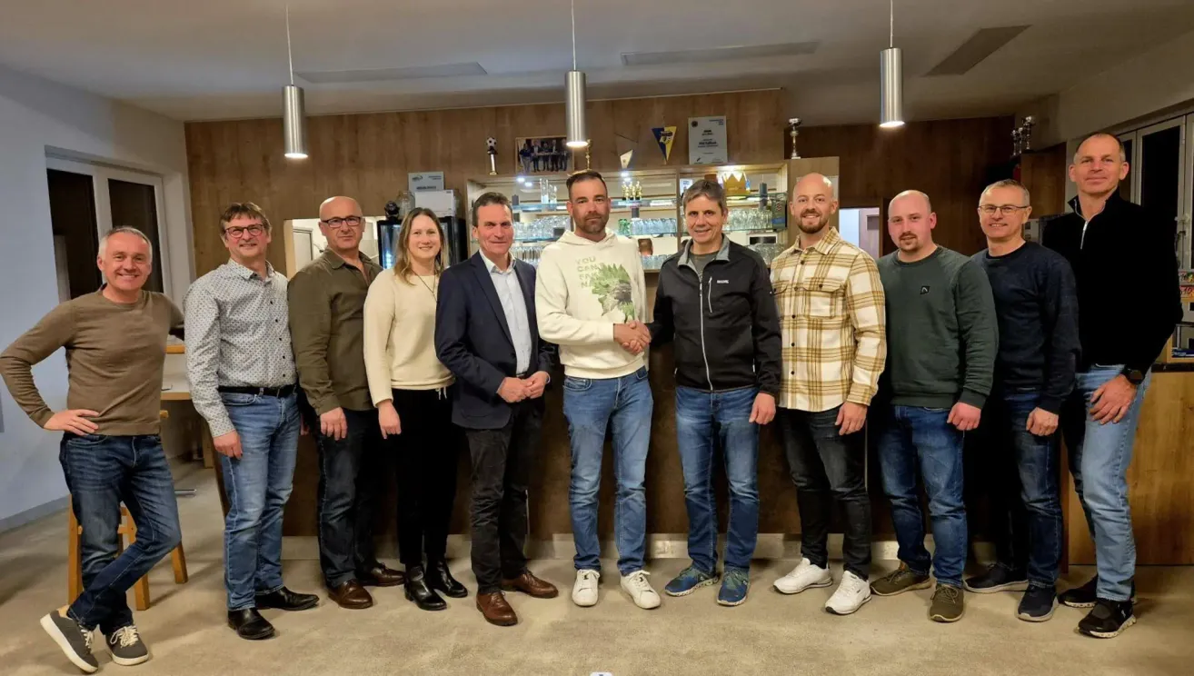 Eine Gruppe von Menschen posiert für ein Foto in einer Bar. Sie stehen hinter einer Theke mit Regalen und einem Pokal.