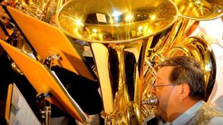 Ein Mann spielt ein großes Messinginstrument mit goldener Oberfläche, möglicherweise eine Tuba, inmitten einer Gruppe von Musikern.