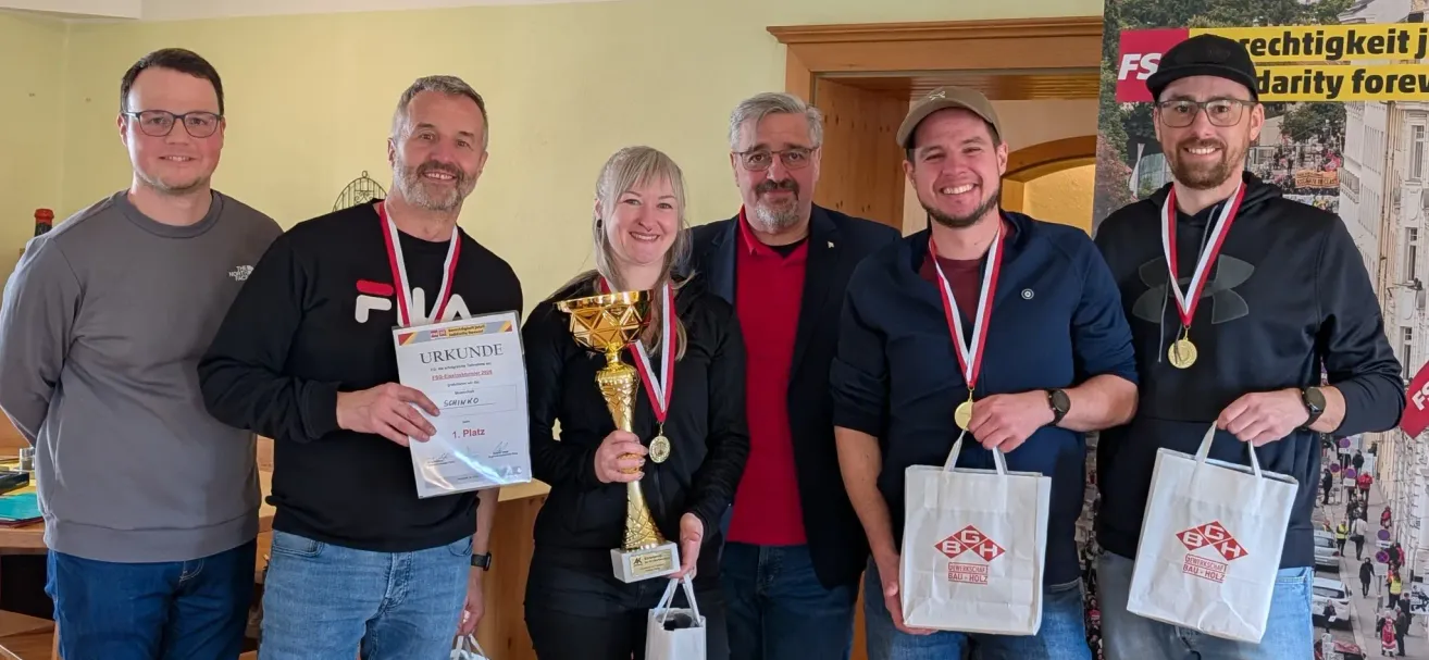 Vier Personen posieren für ein Foto mit Medaillen und Trophäen; eine Frau hält eine goldene Trophäe und ein Mann rechts hält eine weiße Tasche.