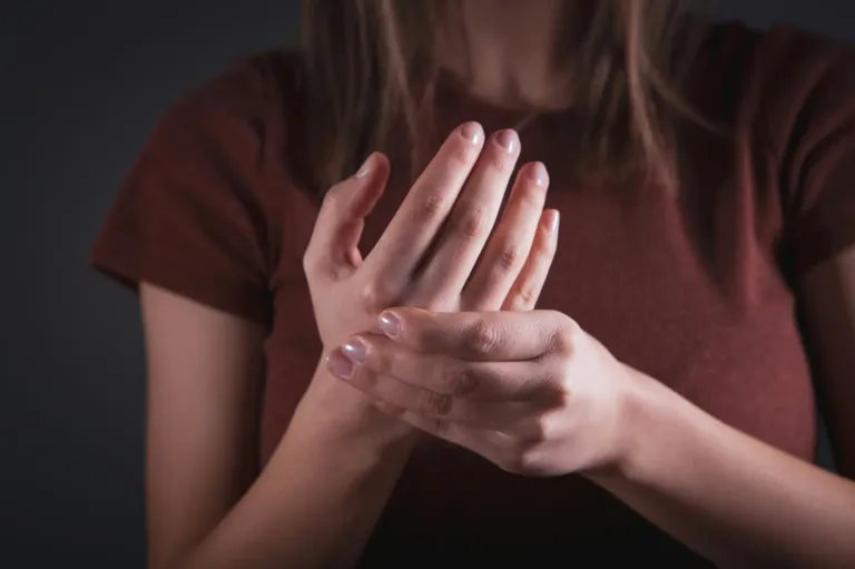 Eine Frau mit langen Haaren und einem braunen Shirt macht eine Handgeste mit ihren Fingern.