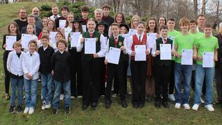 Eine Gruppe von Menschen steht auf einem Rasenfeld und hält Urkunden in der Hand. Sie alle lächeln und scheinen für ein Foto zu posieren.