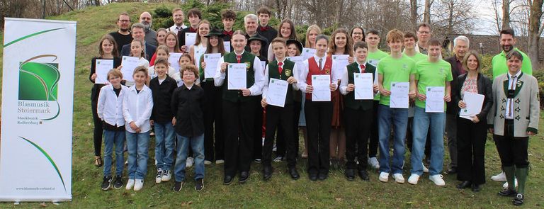 Eine Gruppe von Menschen steht auf einem Rasenfeld und hält Urkunden in der Hand. Sie alle lächeln und scheinen für ein Foto zu posieren.