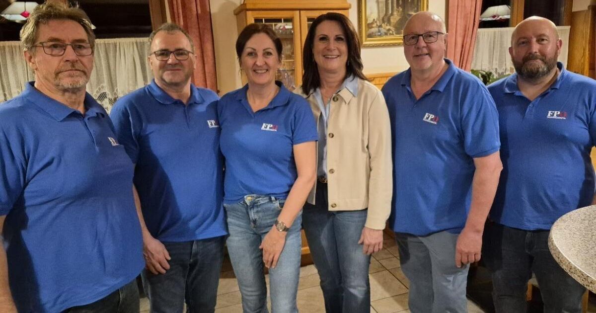 Fünf Personen, drei Männer und zwei Frauen, stehen in einem Raum zusammen. Sie tragen blaue Polo-Shirts mit den Buchstaben 'FP' und einem Logo darauf. Sie lächeln für ein Foto.