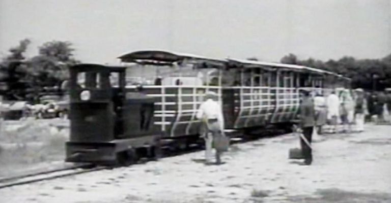 Ein altertümlicher Zug mit einem Mann, der eine Tasche hält, und einem anderen Mann, der ein Werkzeug auf den Gleisen hält.