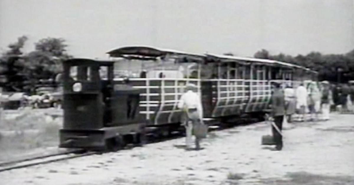 Ein altertümlicher Zug mit einem Mann, der eine Tasche hält, und einem anderen Mann, der ein Werkzeug auf den Gleisen hält.