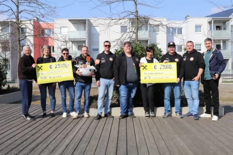 Eine Gruppe von Menschen steht draußen und hält gelbe Schilder mit Geldbeträgen. Das Schild auf der linken Seite zeigt '29.000€', und das auf der rechten Seite zeigt '29.000€'. Sie sind alle in Schwarz gekleidet.