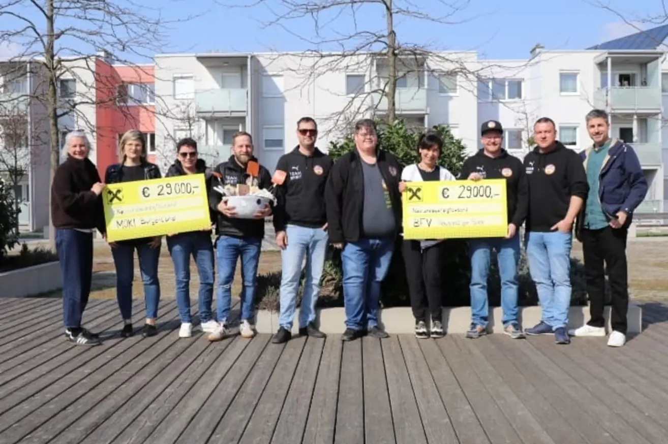 Eine Gruppe von Menschen steht draußen und hält gelbe Schilder mit Geldbeträgen. Das Schild auf der linken Seite zeigt '29.000€', und das auf der rechten Seite zeigt '29.000€'. Sie sind alle in Schwarz gekleidet.