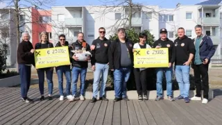 Eine Gruppe von Menschen steht draußen und hält gelbe Schilder mit Geldbeträgen. Das Schild auf der linken Seite zeigt '29.000€', und das auf der rechten Seite zeigt '29.000€'. Sie sind alle in Schwarz gekleidet.