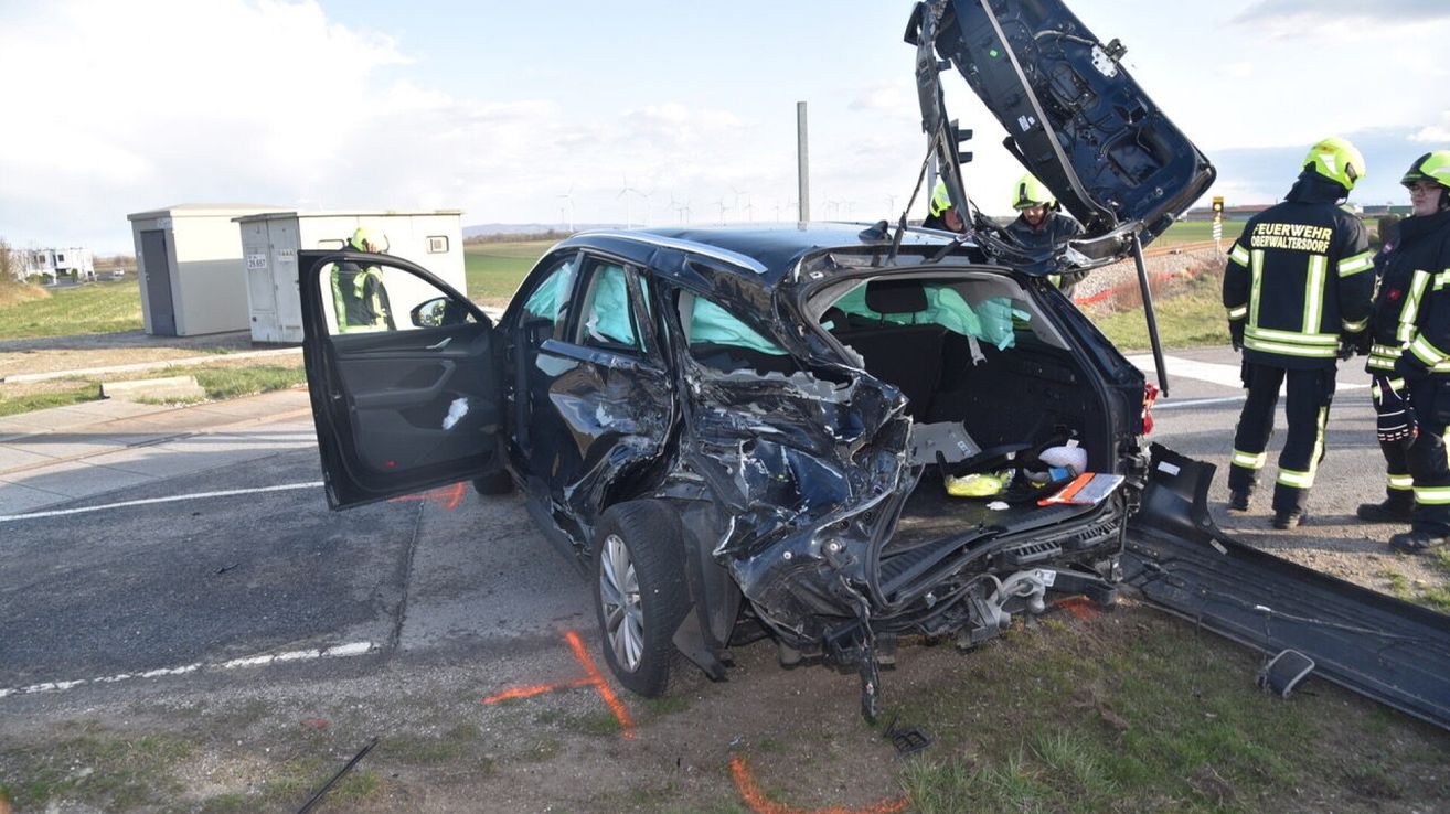 Ein stark beschädigter schwarzer SUV mit offenen Türen und Kofferraum, zwei Personen in Schutzkleidung in der Nähe.