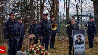 Eine Gedenkfeier mit Polizeibeamten, die um ein Grab stehen, einer von ihnen spricht an einem Podium, mit einem Banner hinter ihm.